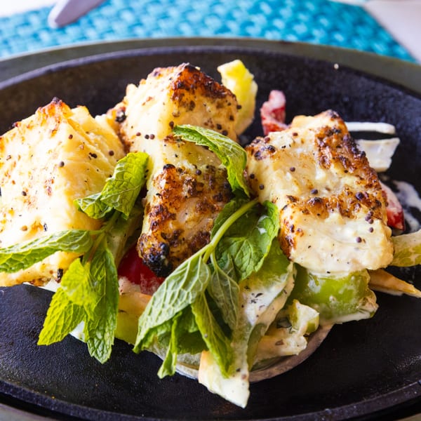 Indian paneer tikka with mint leaves, bell peppers, and creamy sauce on a black plate.