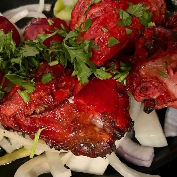 Bright red chicken tikka pieces garnished with fresh cilantro and sliced onions.