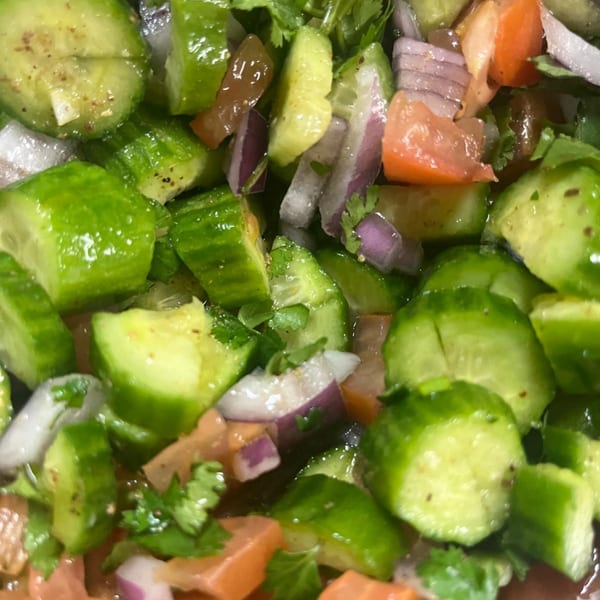 Close-up of a vibrant salad with diced cucumbers, red onions, tomatoes, and fresh cilantro.