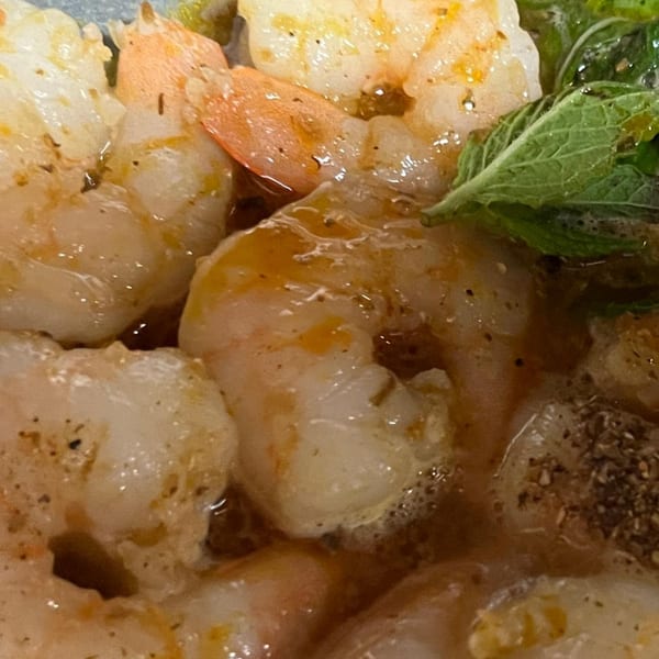 Close-up of cooked shrimp with seasoning and a green herb garnish in a sauce.