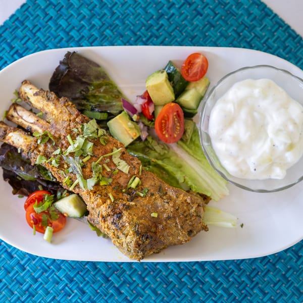 Indian lamb chops with fresh salad and a side of raita on a white plate.